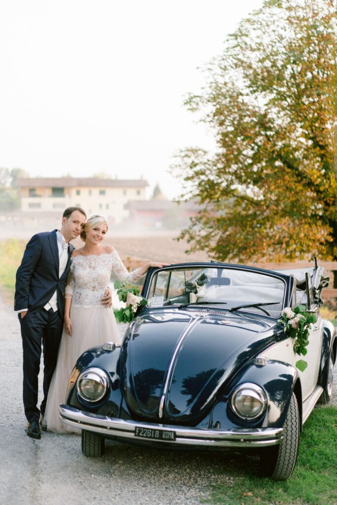 bride and groom posing next to their vintage wedding beetle car
