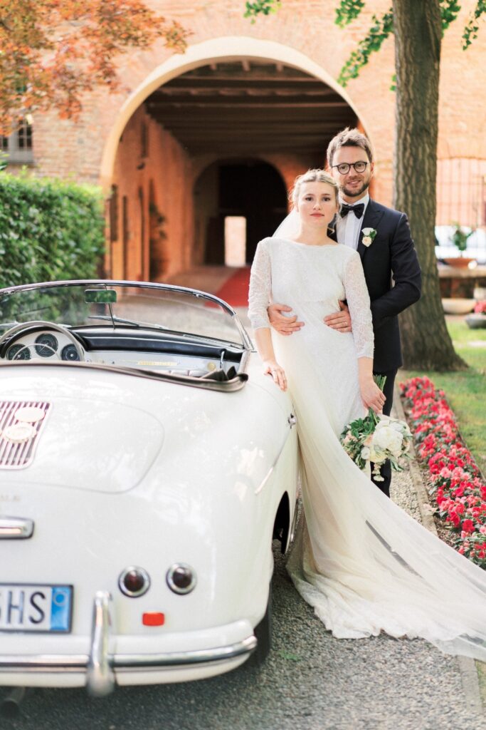 bride and groom pausing over their white vintage car after their luxurious wedding ceremony in italy by atelier crespi wedding planner in italy
