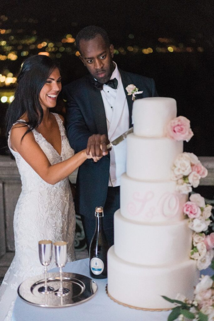 bride and groom cutting their pink wedding cake with roses at a destination wedding planned by atelier crespi wedding planner in italy