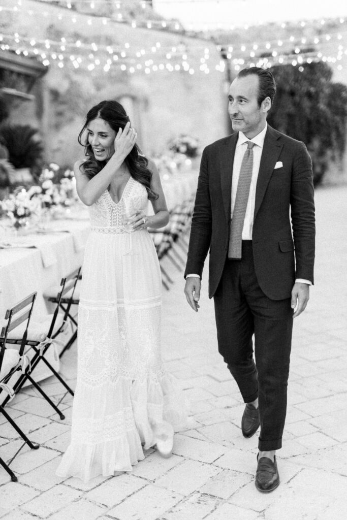 destination wedding in Italy - bride and groom walking through the wedding dinner setting in Tuscany under the fairylights